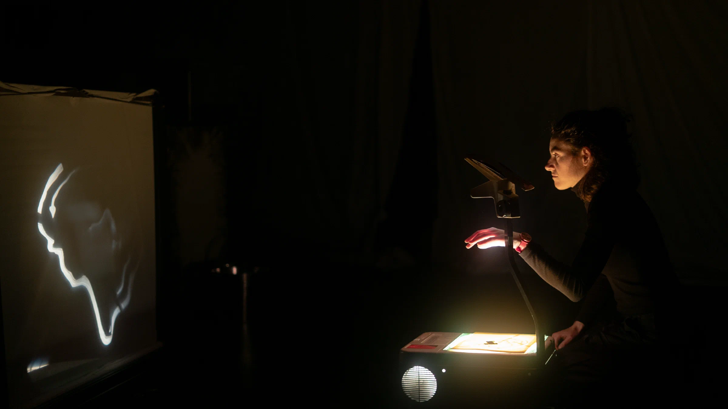 A puppeteer creating a shadow figure with an overhead projector in SWITCHBOARD